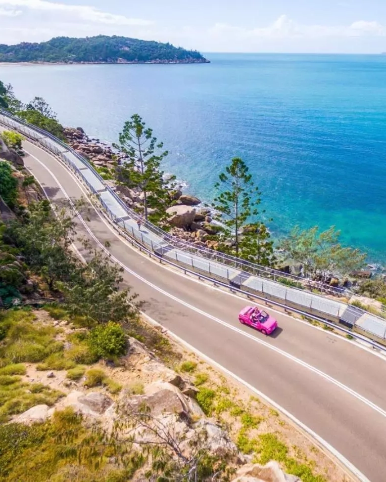 Aerial shot of pink car driving on coastal road, Magnetic Island. Image credit: Townsville Enterprise