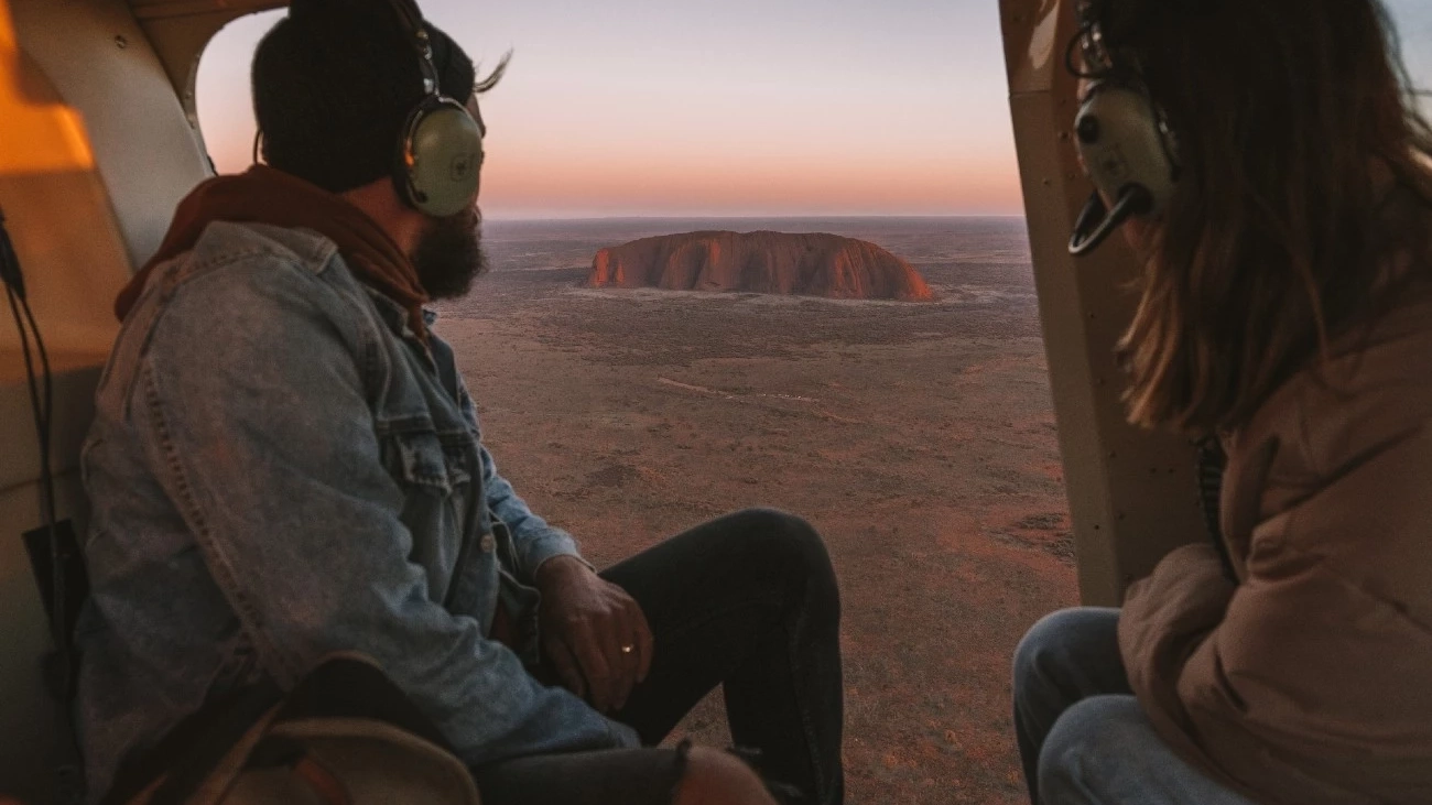 Two people in helicopter looking out over Uluru in the Northern Territory. Image: Tourism NT/Jess Caldwell and Luke Riddle