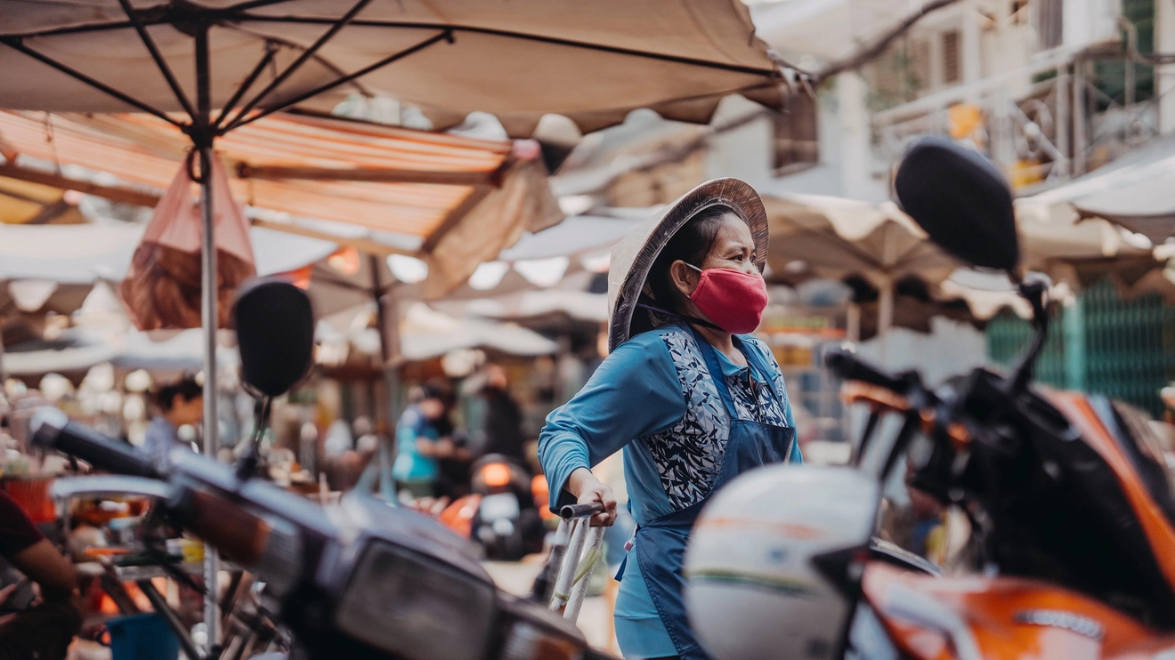 Woman wearing mask and traditional non la straw hat walks through Ho Chi Minh City’s bustling Chinatown. Image credit: stock.adobe.com
