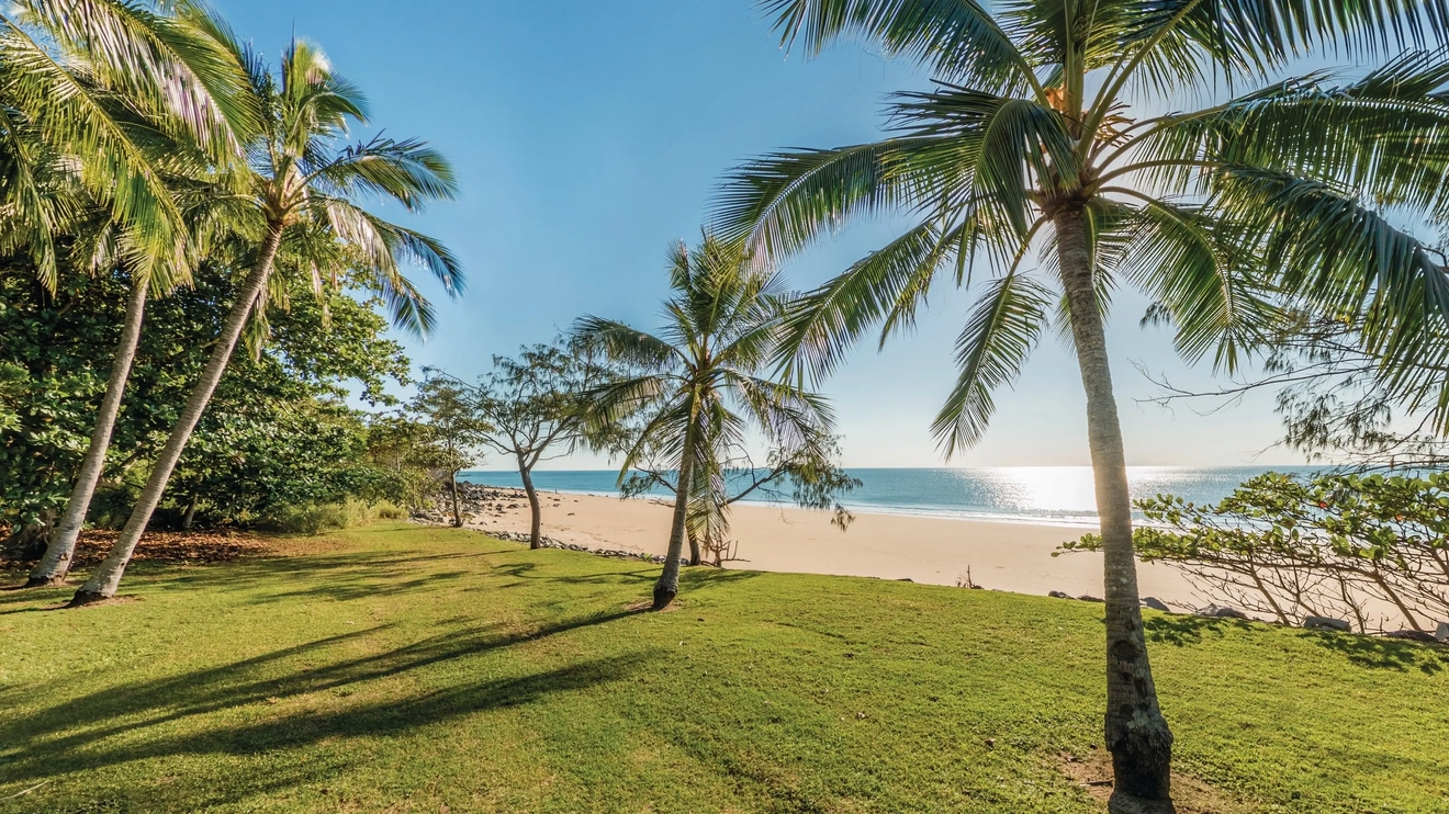 Padang rumput dan pohon palem berjajar di pasir putih dan air yang tenang di Blacks Beach, Mackay. Kredit foto: Tourism and Events Queensland