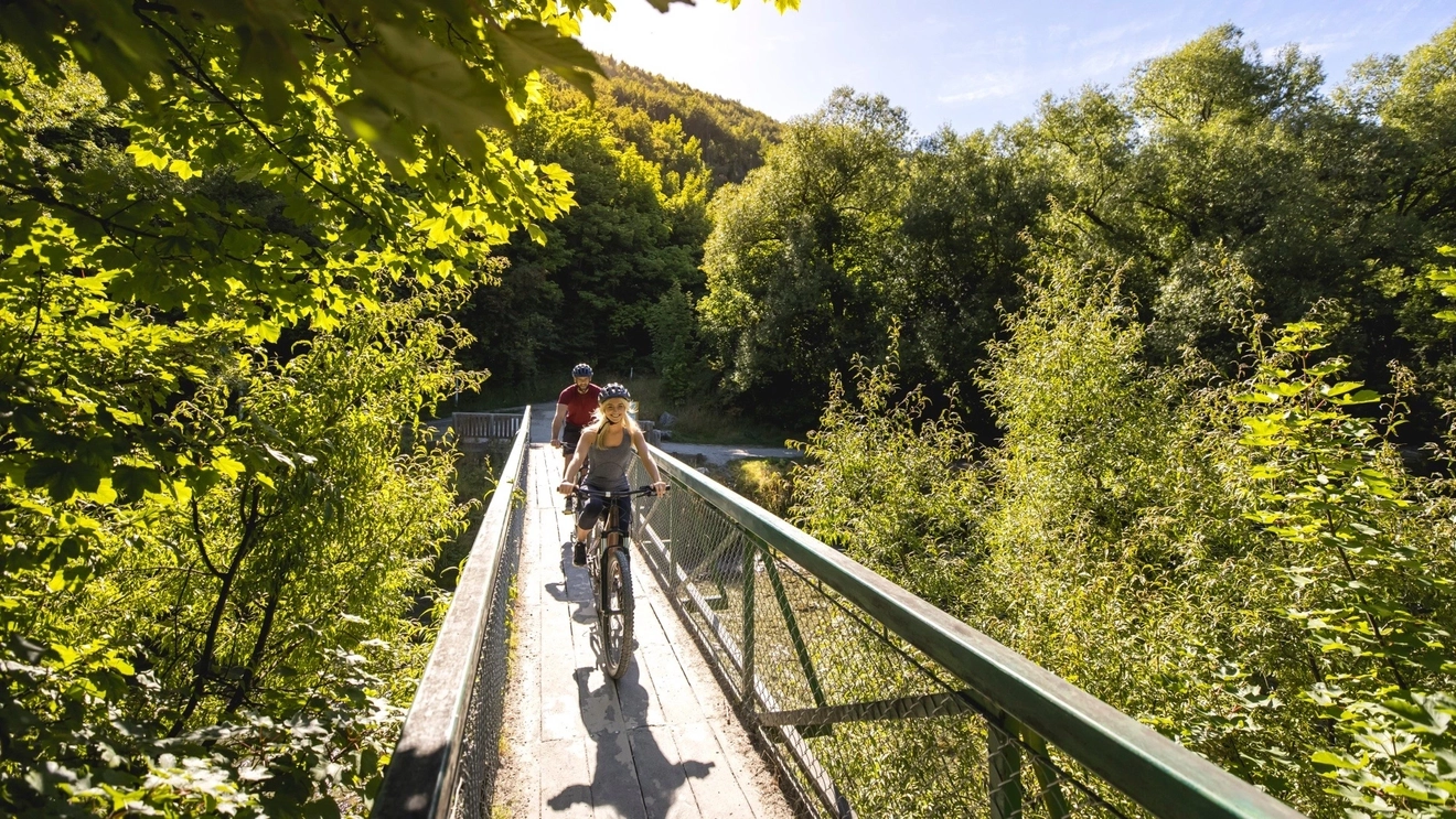 Two people on bikes, cycling through greenery in Arrowtown, near Queenstown, New Zealand. Image credit: QueenstownNZ.co.nz/Miles Holden