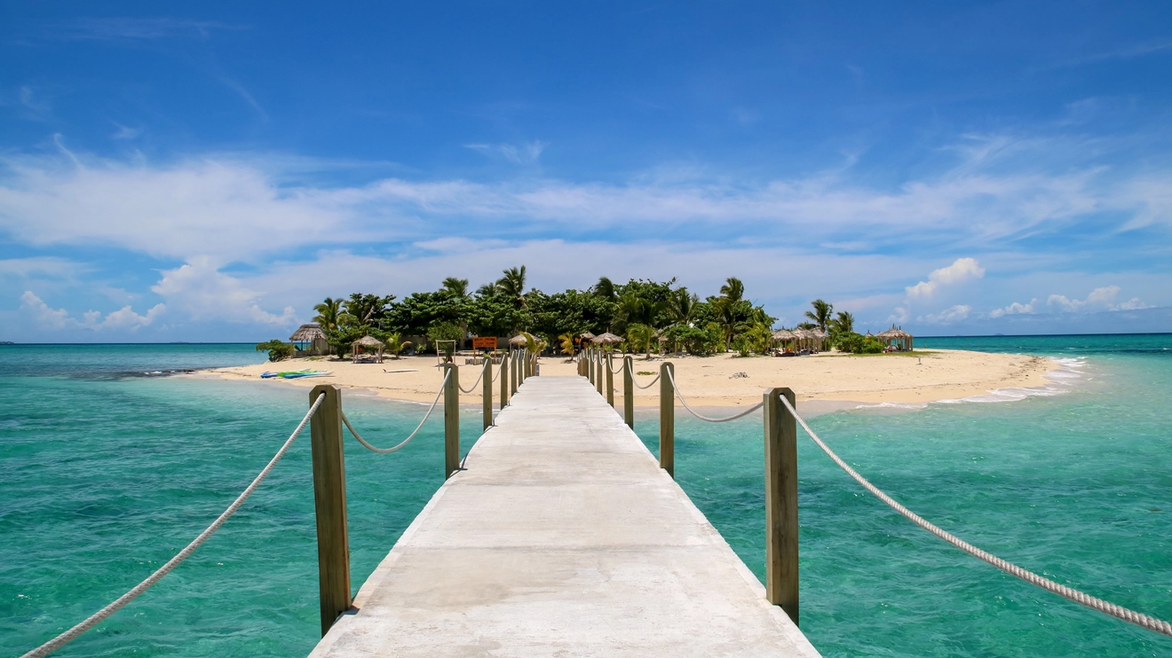 Pier leading to tropical Tivua Island in Fiji with clear blue sky, palm trees, white sand and turquoise crystal clear water. Image credit: Shutterstock