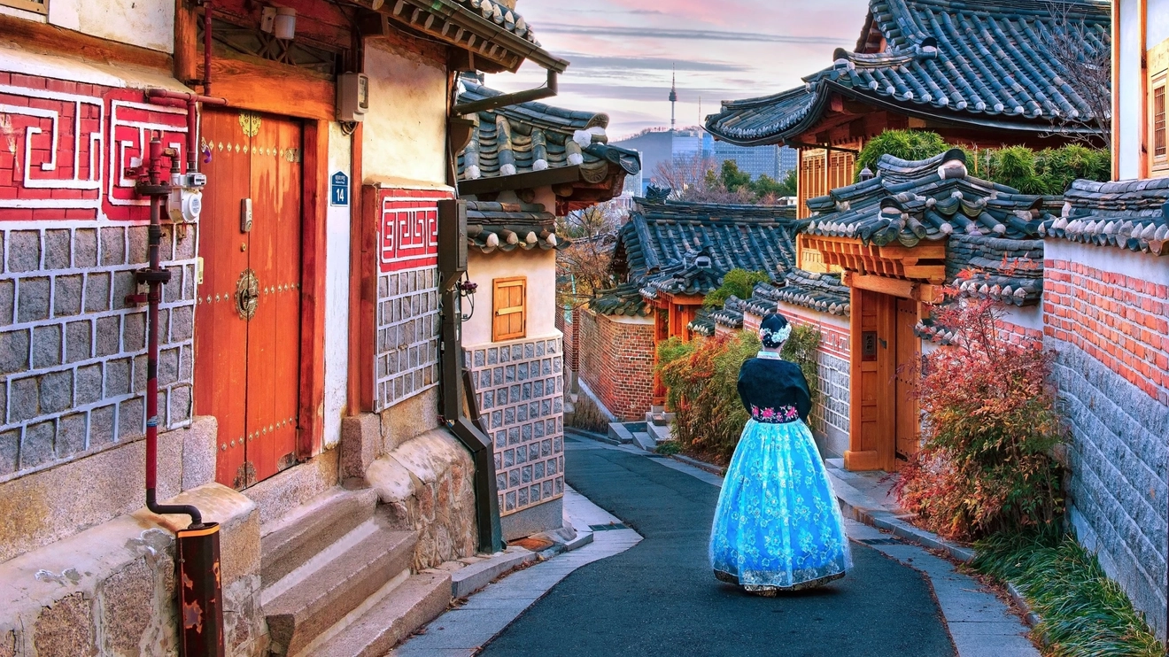 Woman in traditional dress standing in laneway lined with old wooden houses in Bukchon Hanok Village, Seoul, South Korea. Image credit: stock.adobe.com