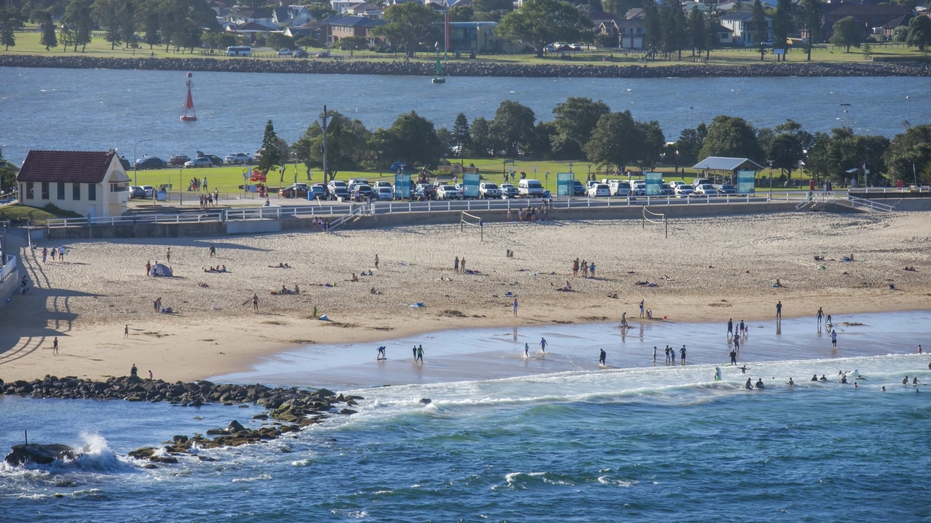 Aerial view of water and sand and people enjoying Nobbys Beach, Newcastle. Image credit: Destination NSW