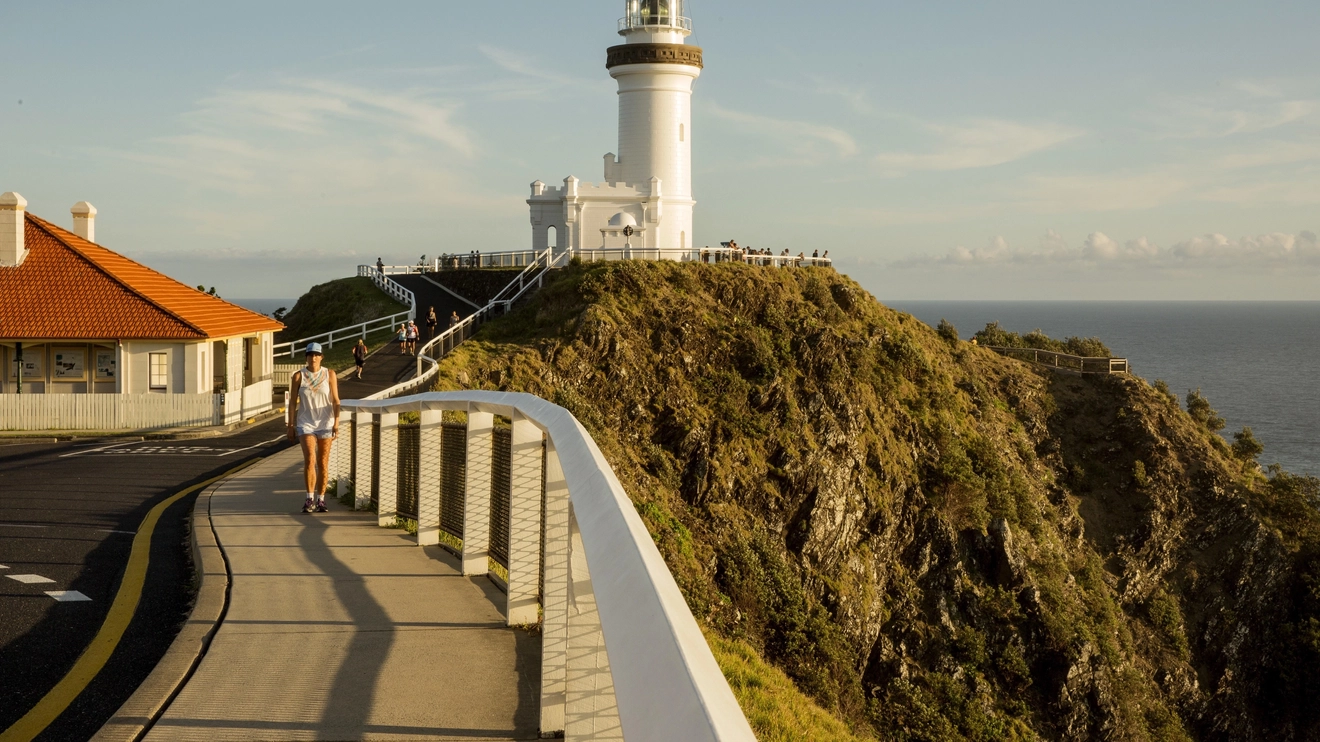 A walking track on a sunny day, with the Cape Byron Lighthouse in the background. Image credit: Destination NSW