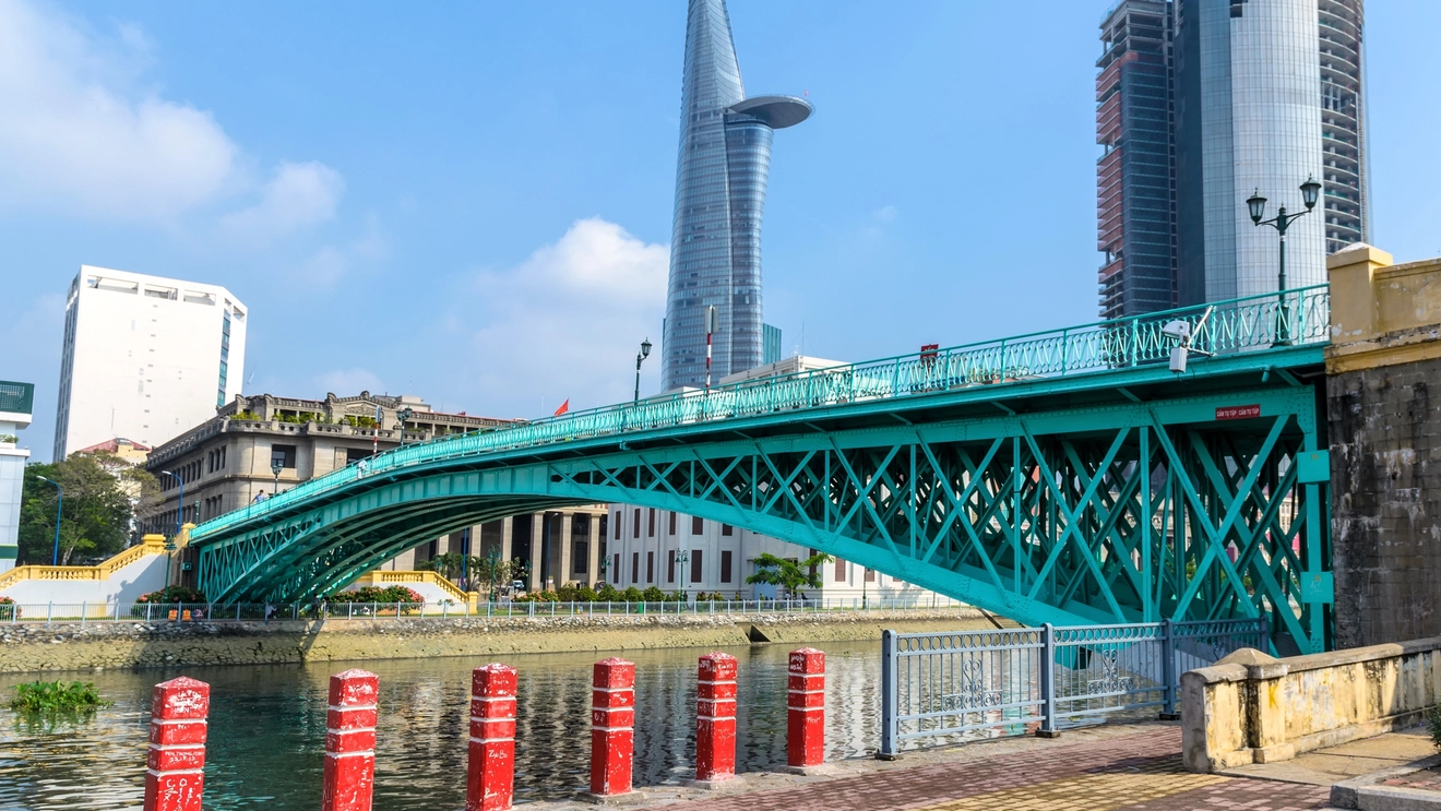Blue steel Rainbow Bridge over the Saigon River with skyscrapers in background, in Ho Chi Minh City. Image credit: stock.adobe.com