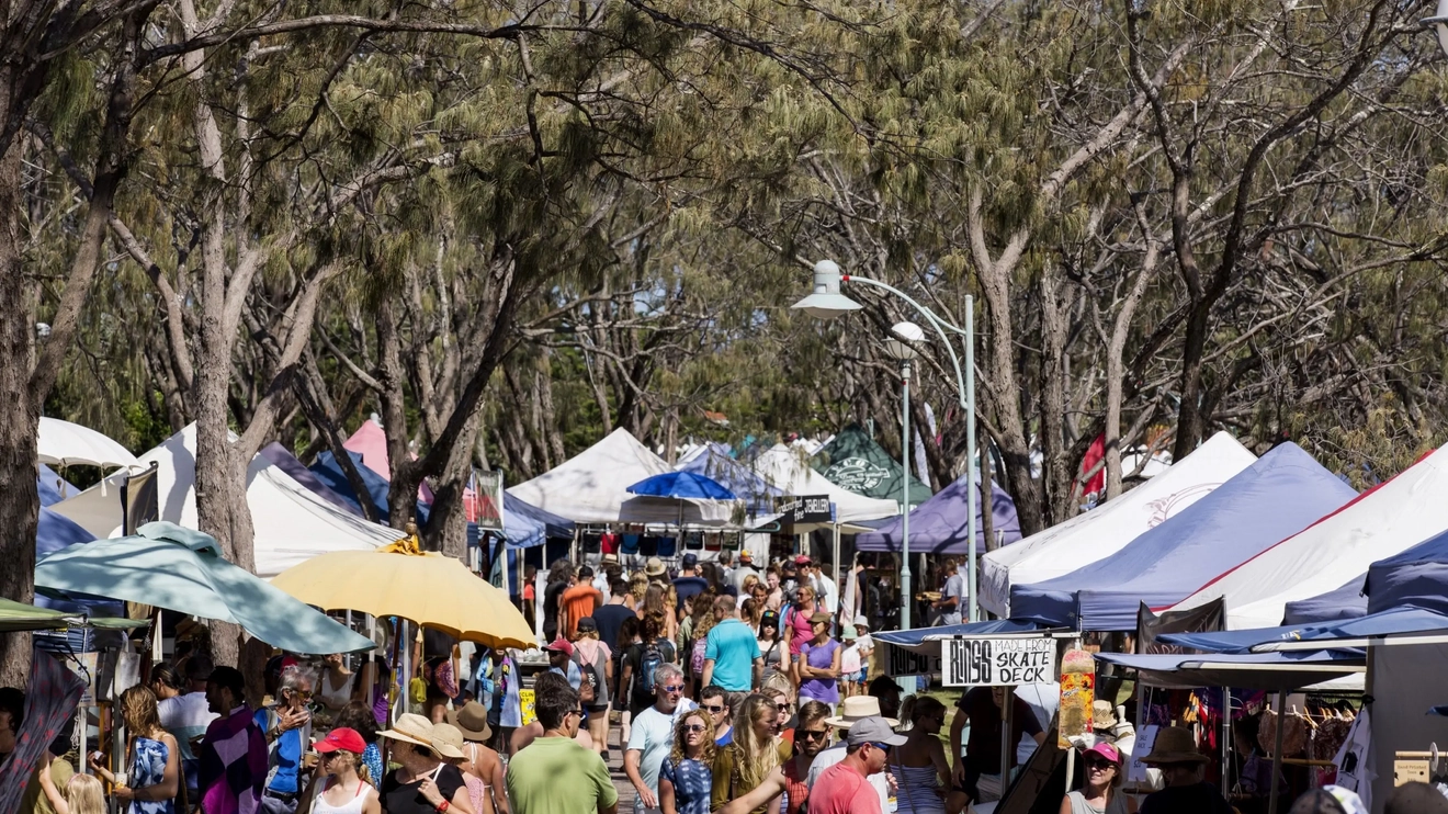 People browsing rows of market stalls surrounded by tall gum trees. Image credit: Destination NSW
