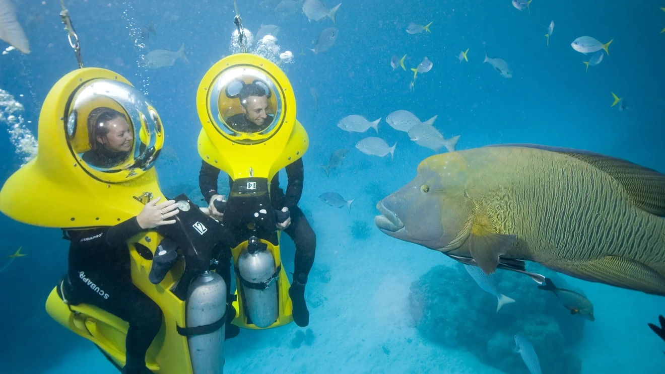 Two people on underwater ride-on scooters come face to face with a large fish in the Great Barrier Reef. Image credit: Scuba Doo Cairns