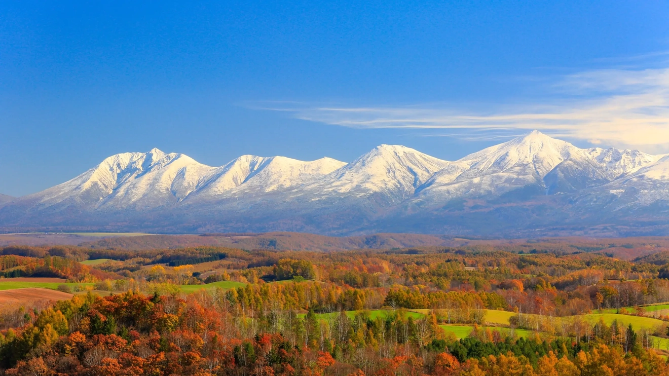 Snowcapped Tokachi mountains with autumn foliage and green fields in the foreground, Furano, Hokkaido, Japan. Image credit: stock.adobe.com