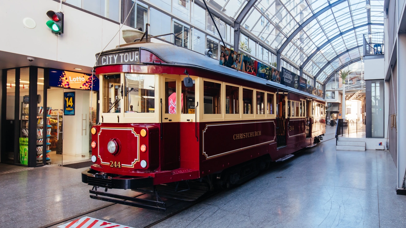 A red tourist tram travels through a shopping arcade in Christchurch, New Zealand. Image credit: FiledIMAGE – stock.adobe.com
