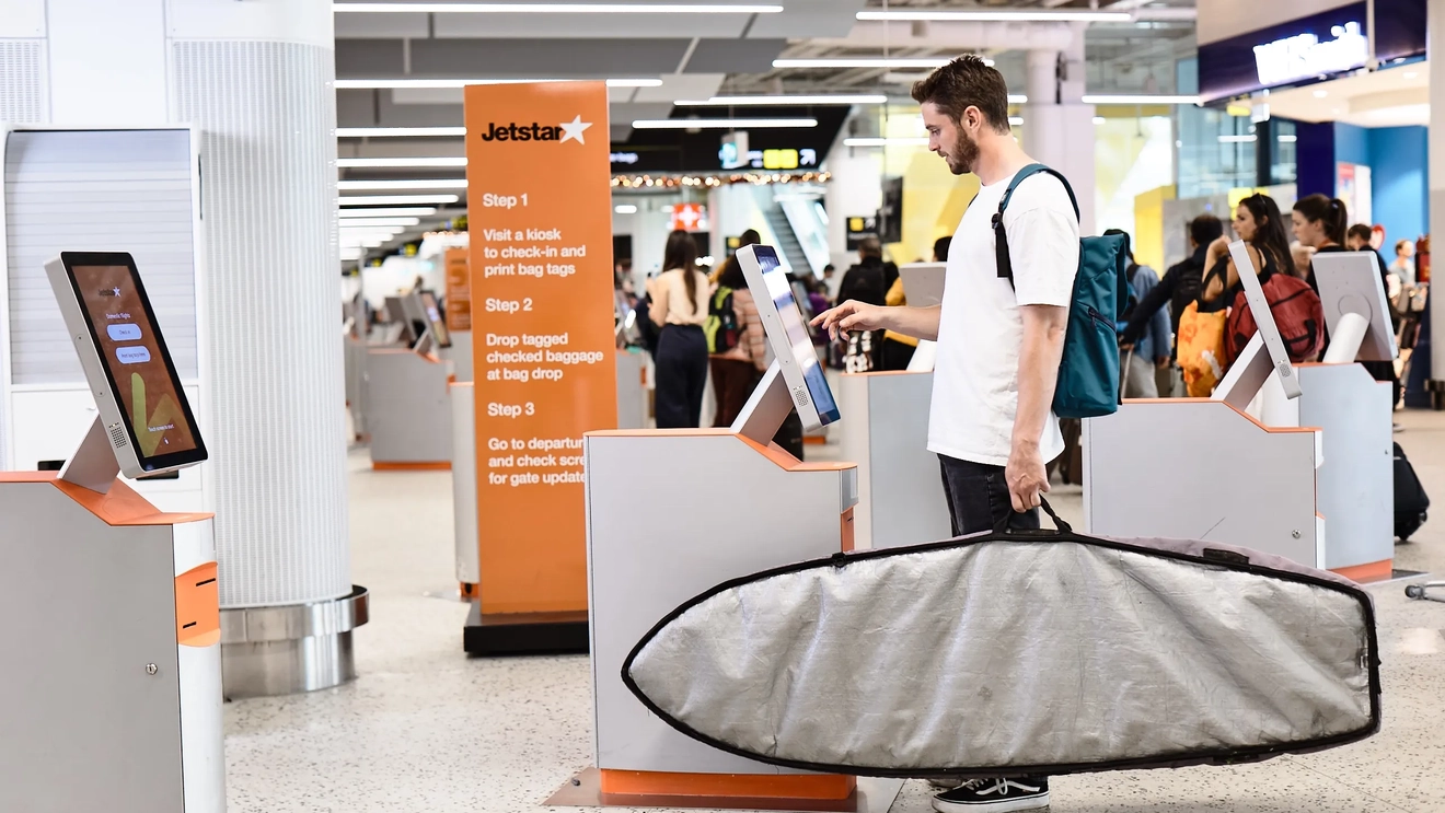 Young man checks in at Jetstar airport kiosk with surfboard.