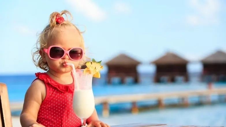 Blonde toddler wearing sunglasses sips from an exotic-looking drink. Get Jetstar's tips on keeping your toddler amused on board.