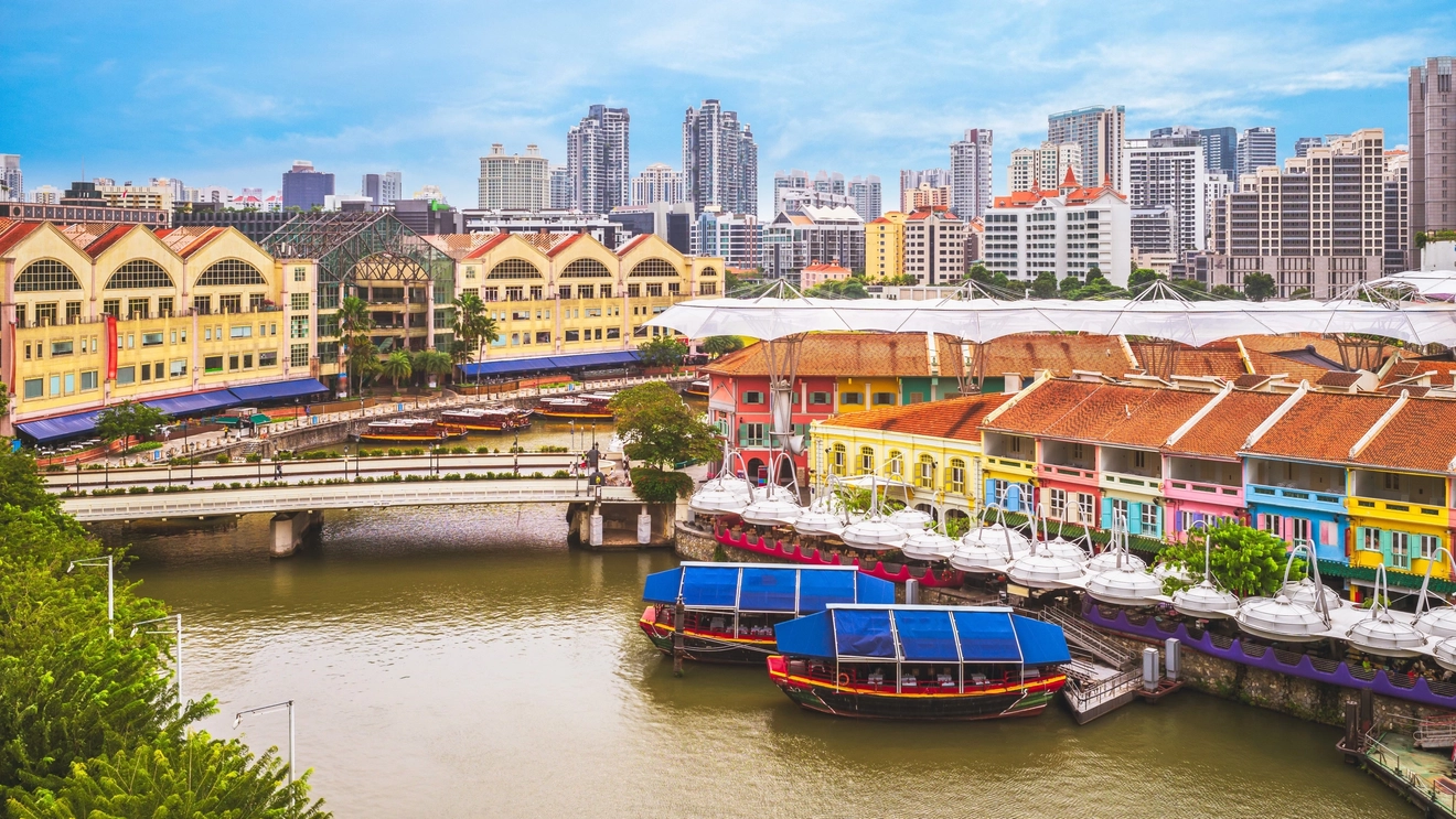 Brightly painted warehouses and outdoor bars line the riverfront, with a bridge across the river and floating restaurants in renovated boats at Clarke Quay, Singapore. Image credit: stock.adobe.com