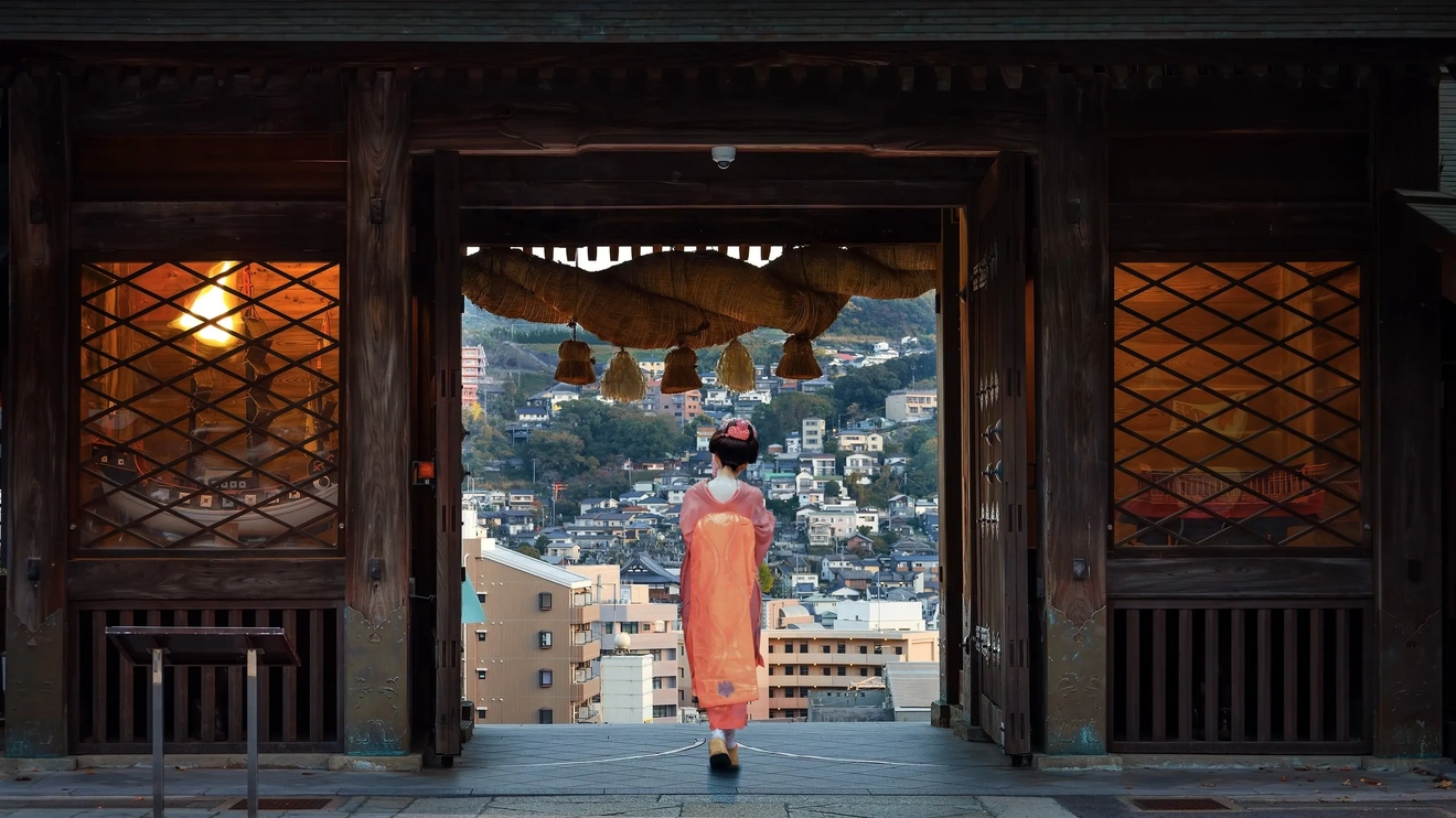 Woman in traditional dress standing at entrance to Suwa Shrine, with Nagasaki city buildings in background, Kyushu, Japan. Image credit: stock.adobe.com