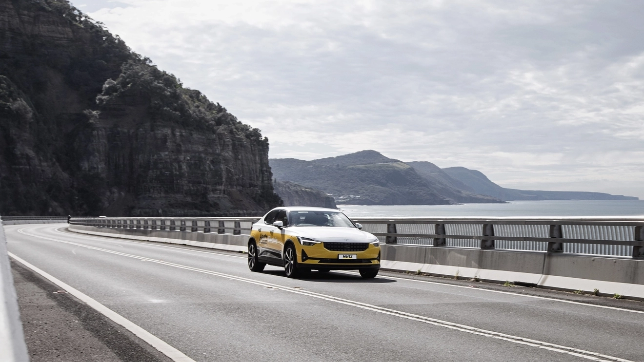 A Hertz electric hire car drives on a coastal road.