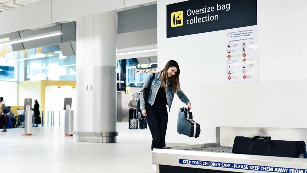 Young woman with long brown hair drops off guitar case at airport oversized baggage carousel