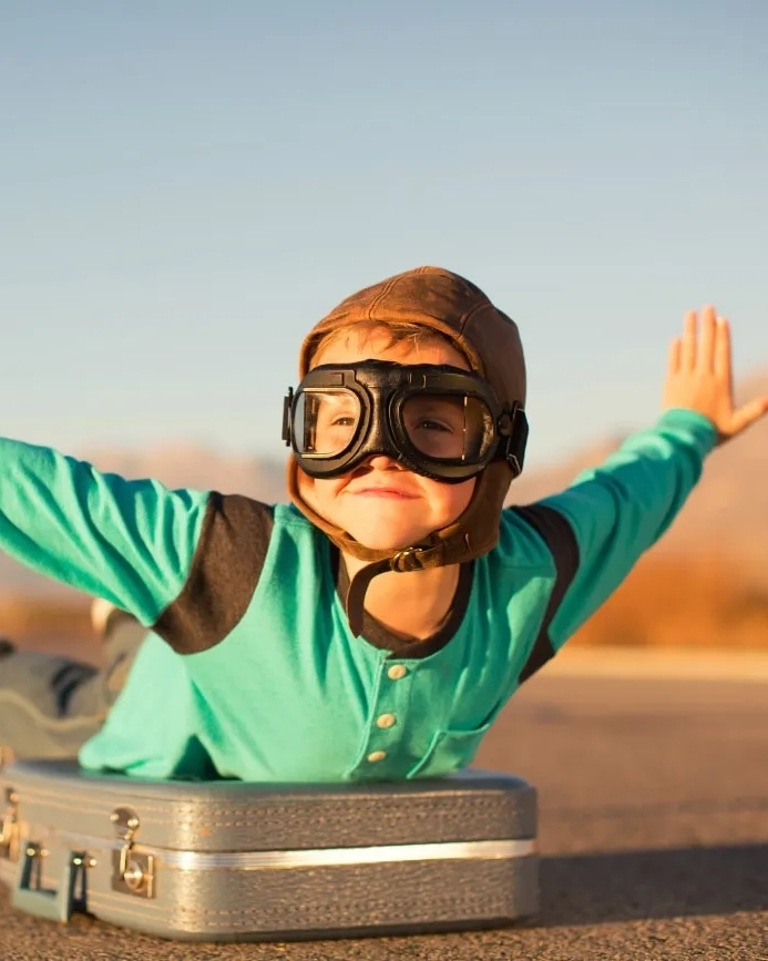 Young boy with goggles imagines flying on suitcase. Image credit: iStock