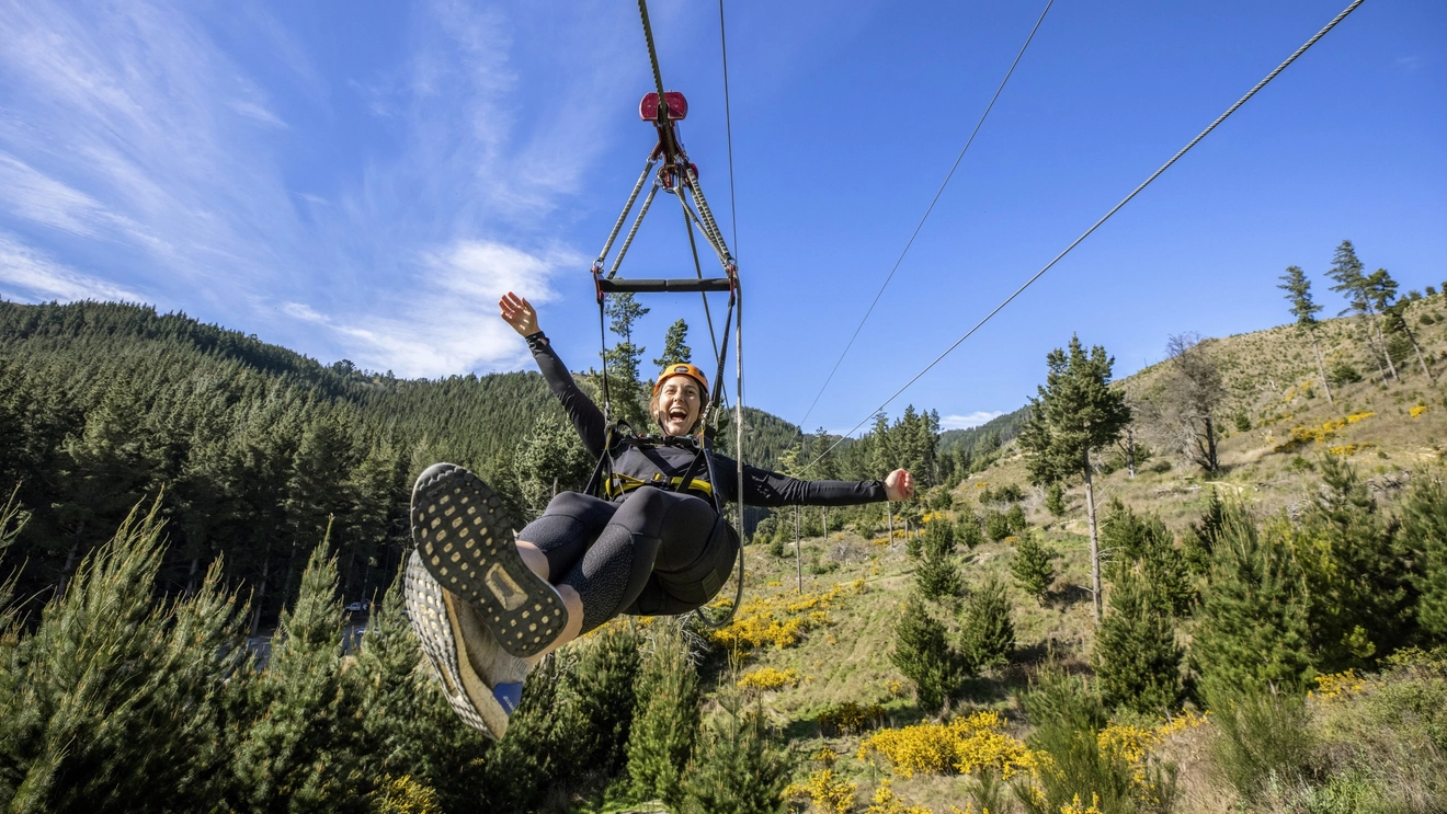 A person in a red helmet laughs as they zipline above a forest on a sunny day, Christchurch Adventure Park, New Zealand. Image credit: Miles Holden