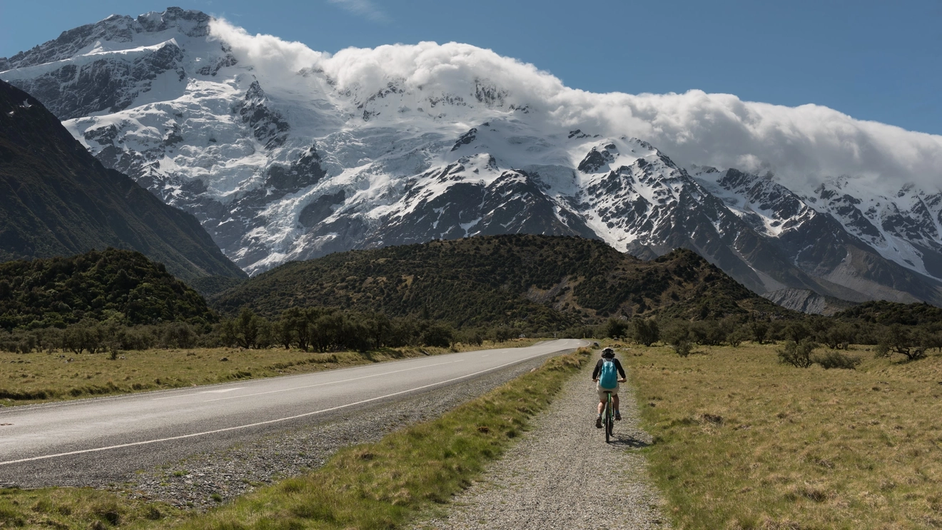 A cyclist rides on a bike path with the Southern Alps ahead, Aoraki Mount Cook National Park, New Zealand.