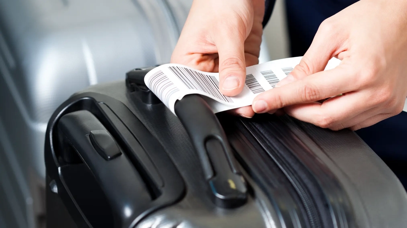 一名男子正在用手将行李标签固定在黑色行李箱把手上。