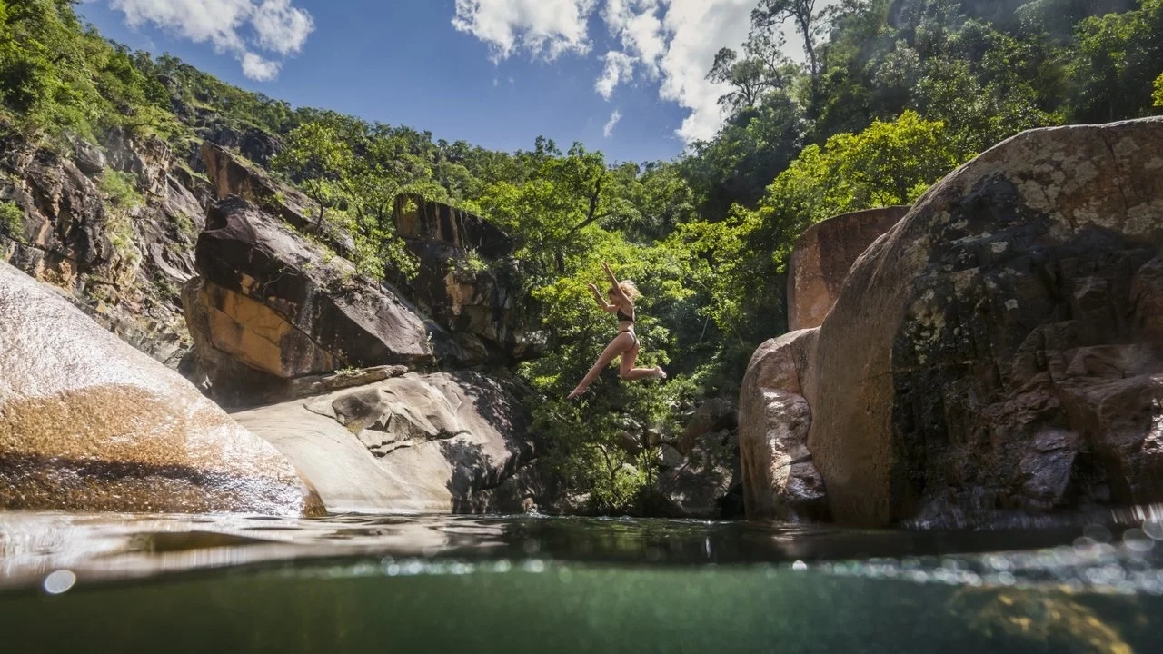 Person jumping into a waterhole surrounded by large boulders. Image credit: Townsville Enterprise