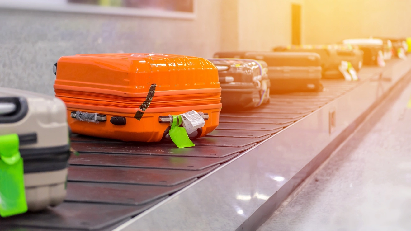 Orange suitcase sits on a baggage collection carousel with some boring grey suitcases.
