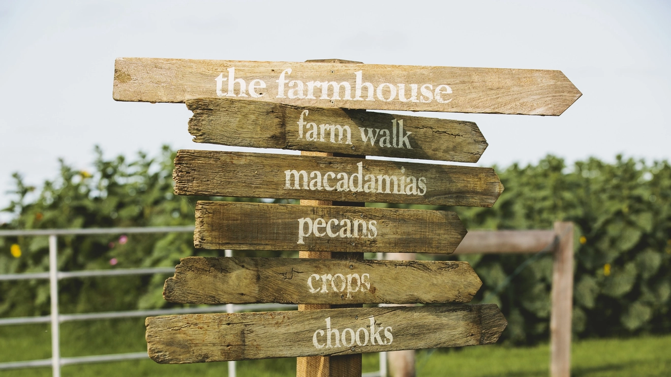 A wooden information sign pointing to different areas of The Farm, Byron Bay. Image credit: Destination NSW