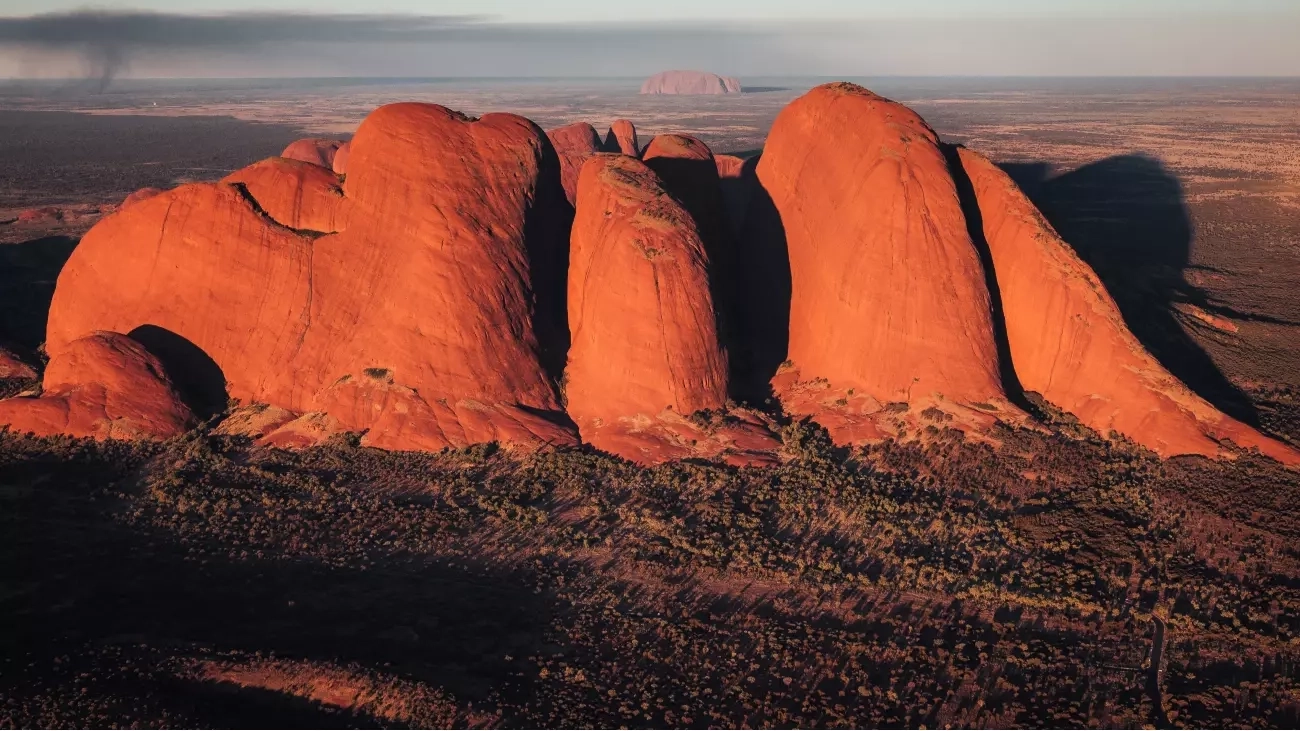 Aerial view of Kata Tjuta at sunrise, with Uluru in the background. Image: Tourism NT/Jason Charles Hill