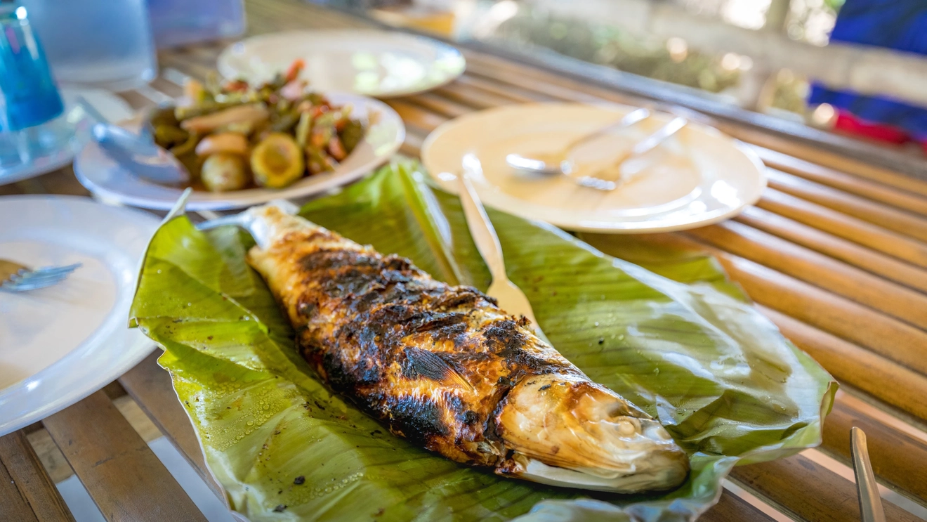 A grilled bangus, also known as milkfish, served on a banana leaf, on a table with other dishes. Image credit: stock.adobe.com