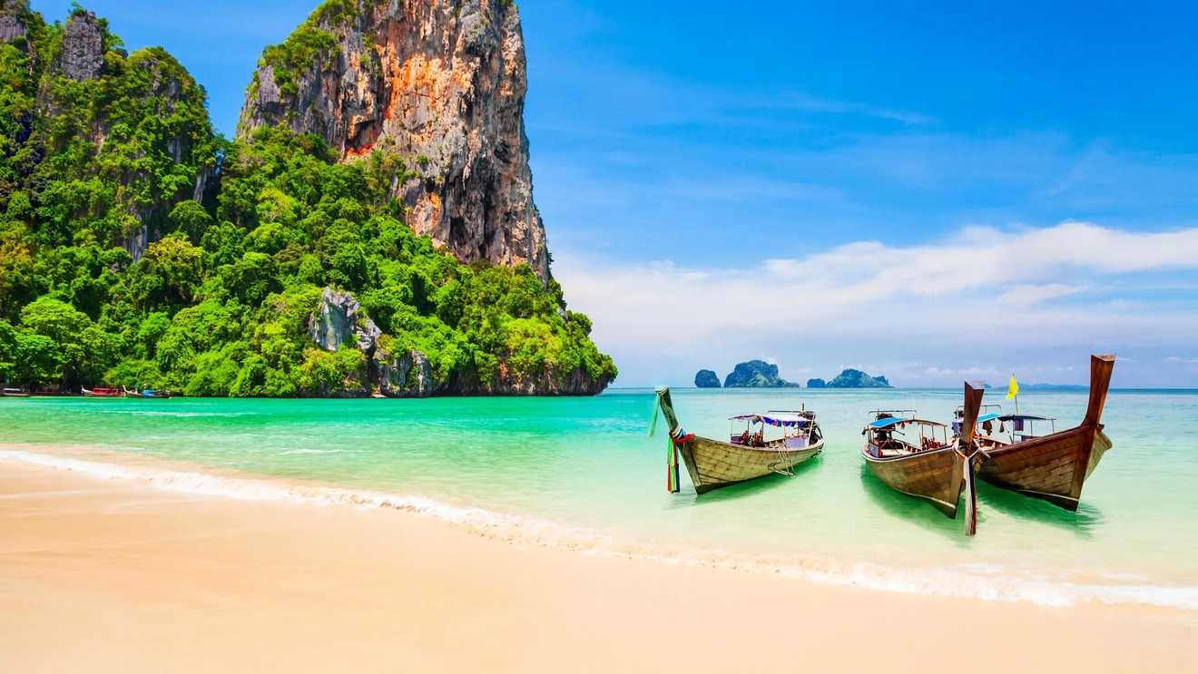 Ba chiếc thuyền đuôi dài neo bên bãi biển và phía xa là những mỏm đá vôi cùng những hòn đảo, Thái Lan. Hình ảnh của: stock.adobe.com