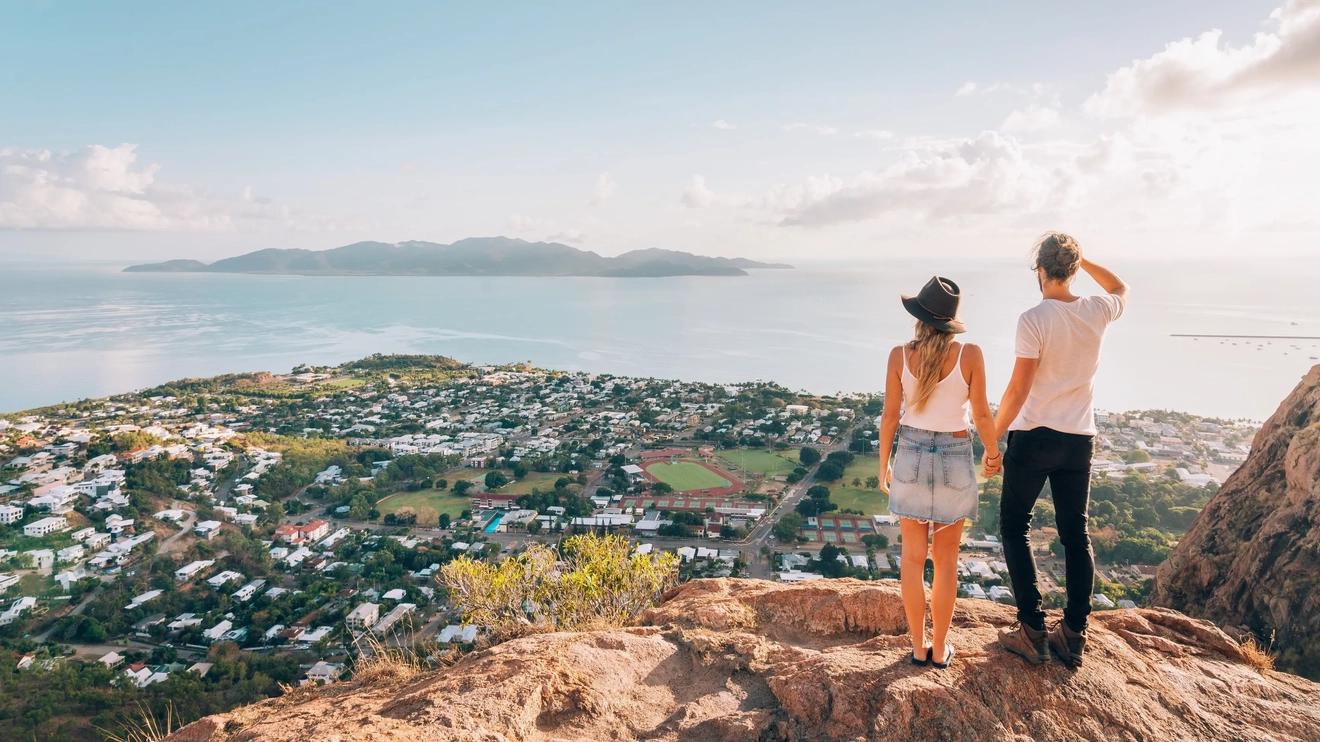 Pemandangan dari belakang pasangan yang mengagumi pemandangan Townsville dan Magnetic Island dari Castle Rock. Kredit foto: Tourism and Events Queensland