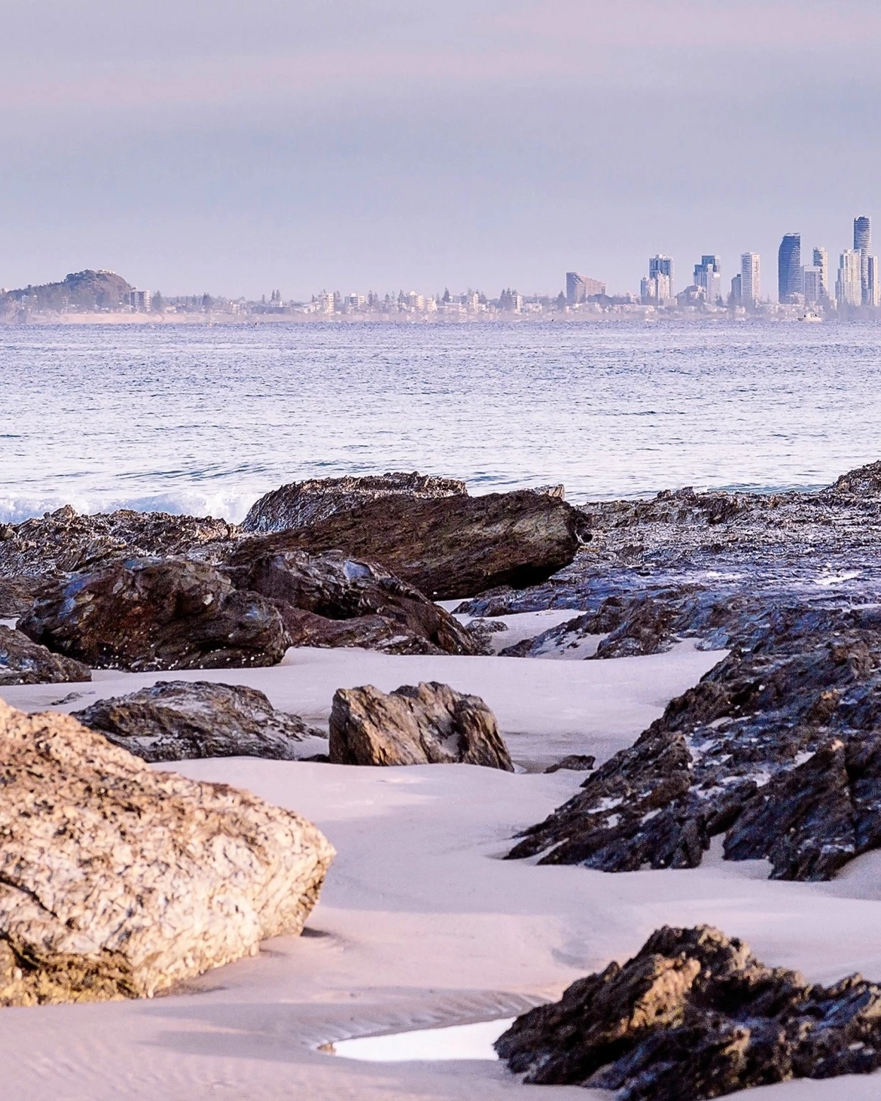 Currumbin Beach with stand-up paddleboarders on the water and city skyline in the background, Gold Coast, Queensland. Image credit: Destination Gold Coast