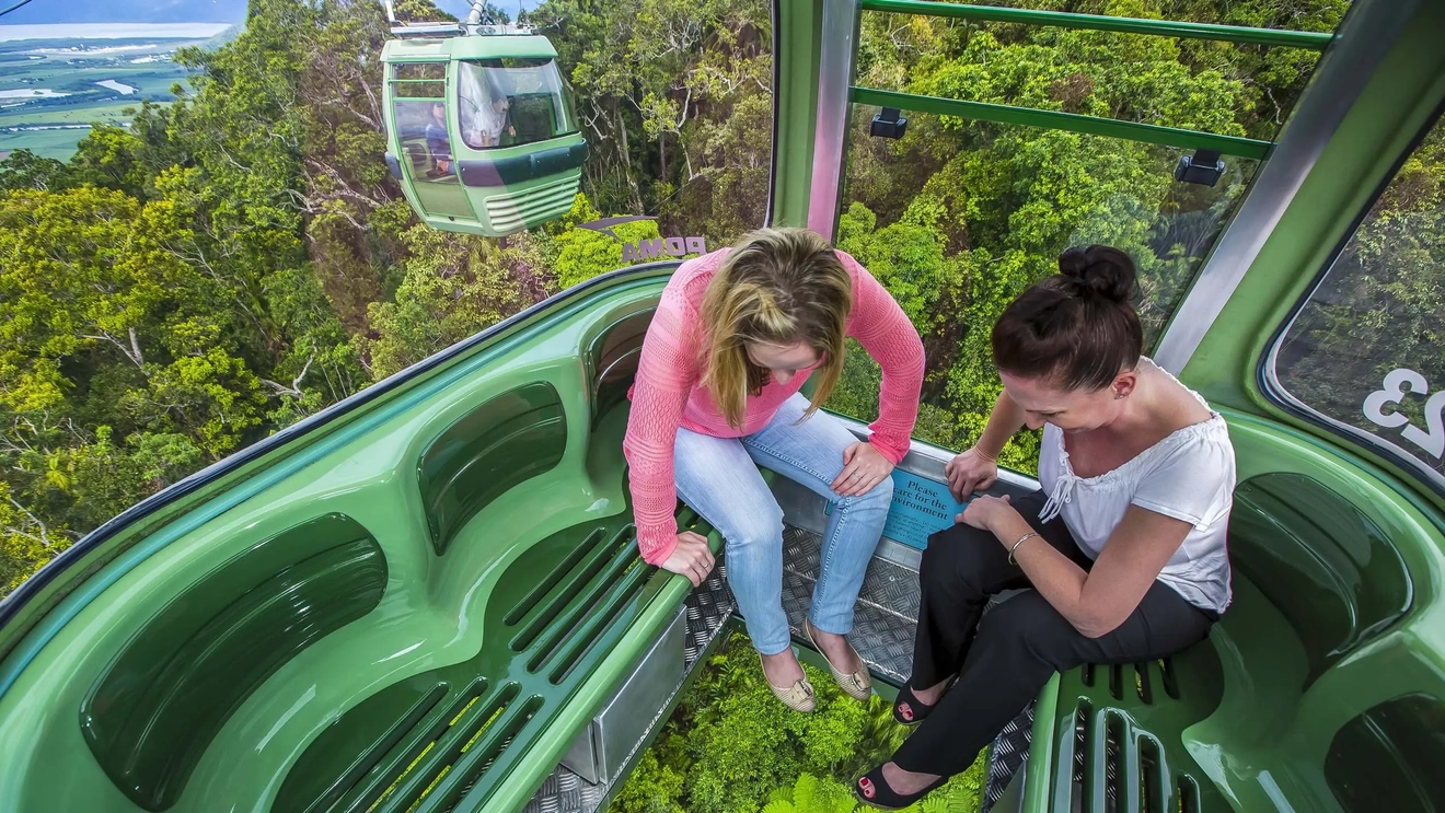 Two people sitting in a Skyrail gondola look at the rainforest below through the glass flooring. Image credit: Skyrail Rainforest Cableway